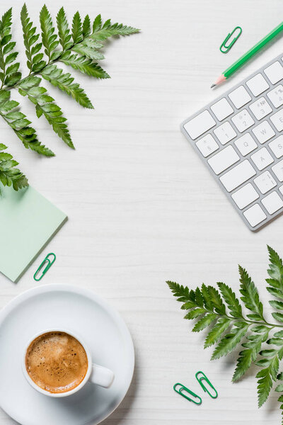 elevated view of coffee cup, fern leaves, stationery and computer keyboard on table 