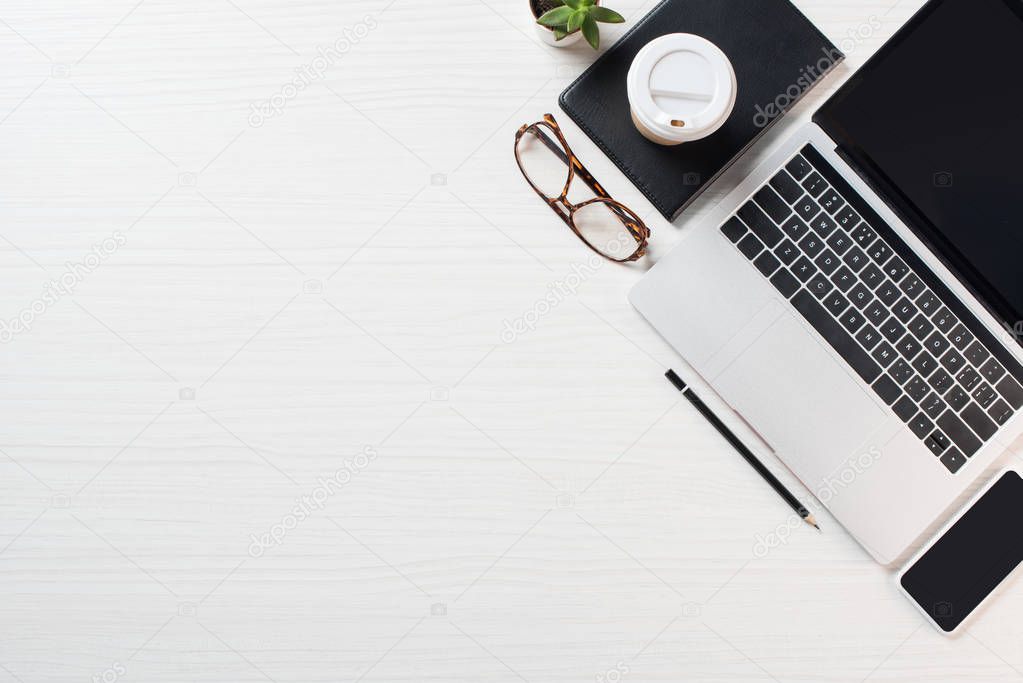 top view of workplace with eyeglasses, coffee and laptop  with blank screen on table 