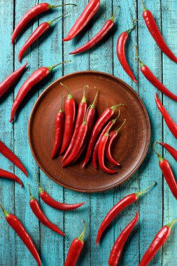 top view of red ripe chili peppers on plate and blue wooden table clipart