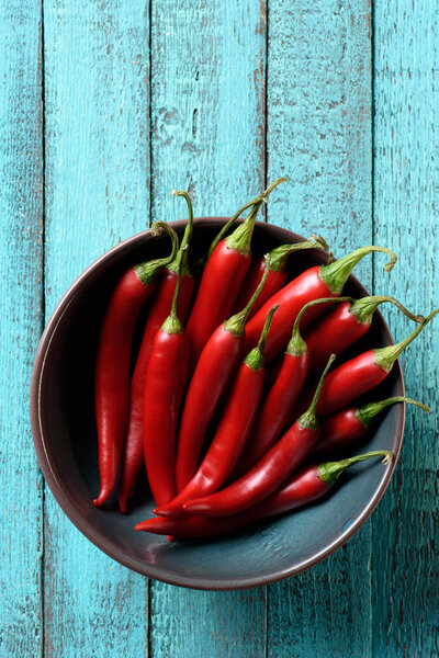 top view of red ripe chili peppers in bowl on blue wooden table
