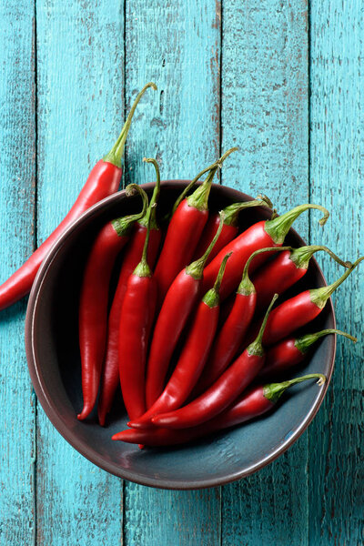 top view of red tasty chili peppers in bowl on blue wooden table