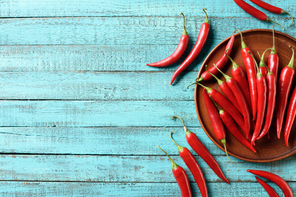 повышенный вид на красный спелый перец чили на тарелке и синий деревянный стол
