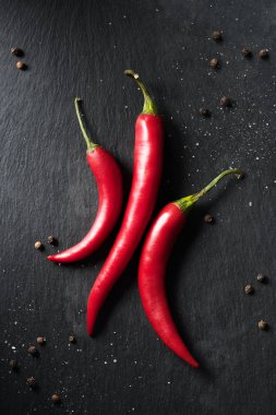 top view of three red ripe chili peppers on black surface clipart