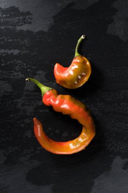 top view of two chili peppers on black surface clipart