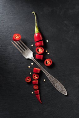 elevated view of cut red ripe chili pepper and fork on black surface clipart