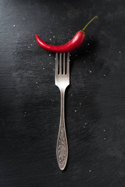 top view of red ripe chili pepper and fork on black surface