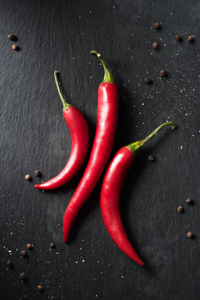 top view of three red ripe chili peppers on black surface