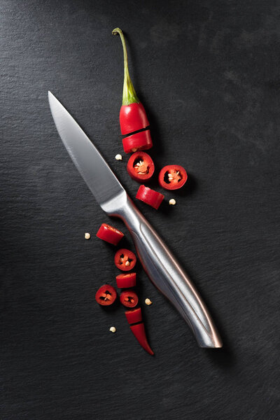 elevated view of cut red ripe chili pepper and knife on black surface