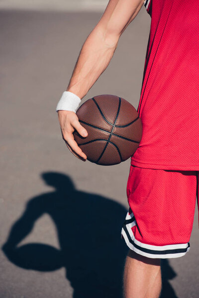 cropped image of sportsman holding basketball ball on street