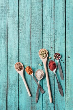 top view of spoons with various dried aromatic spices on turquoise wooden surface  clipart