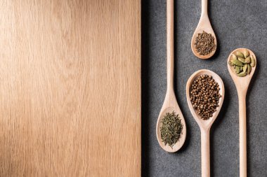 top view of dried spices on wooden spoons and wooden board on grey background clipart