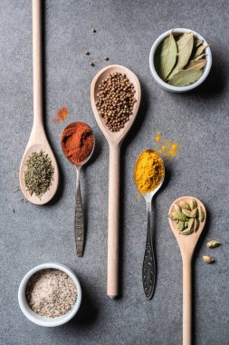 kaşık ve kase içinde farklı kurutulmuş Aromatik baharatlar üstten görünüm gri arka plan üzerinde