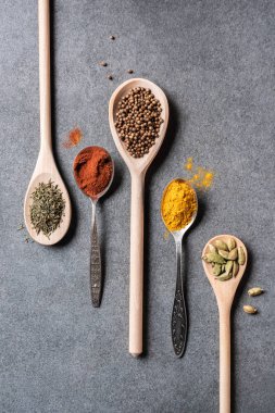 top view of different dried aromatic spices in spoons on grey  background clipart