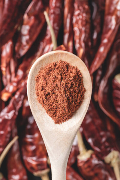 close-up view of wooden spoon with chili powder above red hot chili peppers