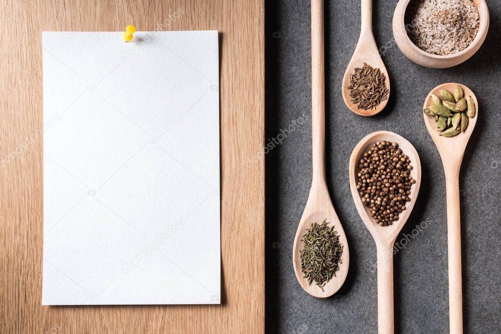 top view of dried spices on wooden spoons and blank paper sheet