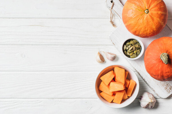 elevated view of pumpkin pieces in bowl, pumpkin seeds and garlic on table 