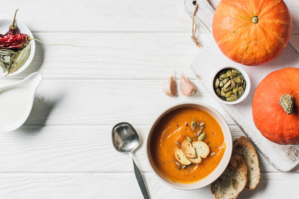 top view of homemade pumpkin soup with rusks, pumpkins and garlic on table 