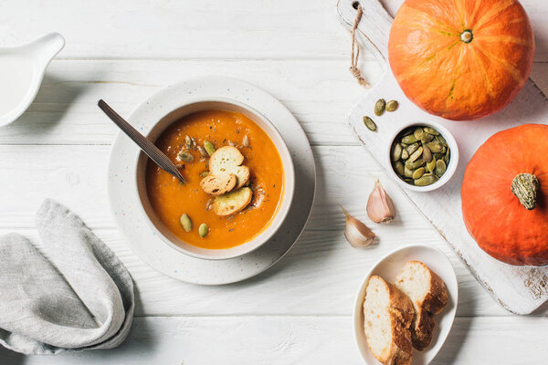 elevated view of pumpkin cream soup with seeds and rusks in bowl on table 