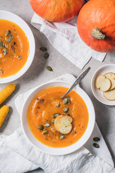 flat lay with corn cobs, pumpkins, rusks and plates with pumpkin cream soup on table 