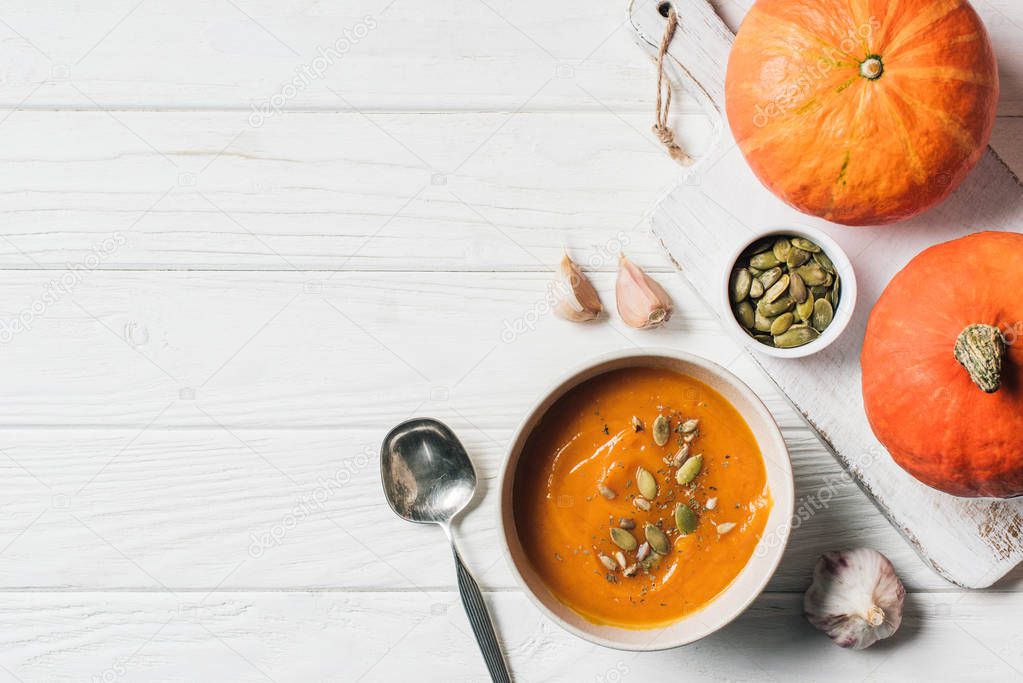 elevated view of pumpkins, garlic and bowl with pumpkin cream soup on table 