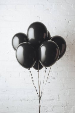 bunch of black balloons on ribbons in front of white brick wall clipart