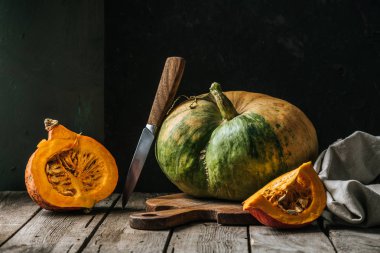 close up view of food composition with pumpkins, knife and cutting board on wooden surface on dark background clipart