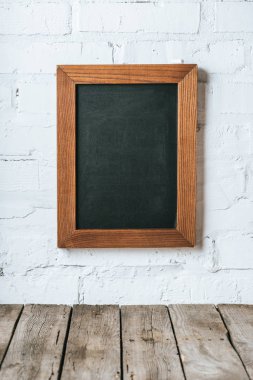 close up view of blank chalkboard on white brick wall and wooden planks surface clipart