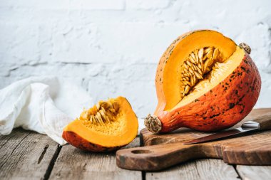 close up view of cut pumpkin on cutting board on wooden surface and white brick wall background clipart