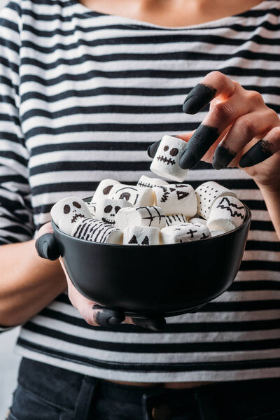 cropped shot of woman holding bowl of marshmallows with skull faces, halloween concept