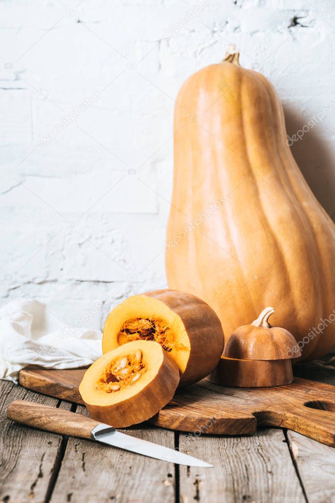 close up view of ripe pumpkins and knife on wooden planks surface and white brick wall background