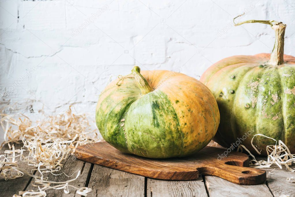 close up view of ripe pumpkins on cutting board on wooden surface and white brick wall background