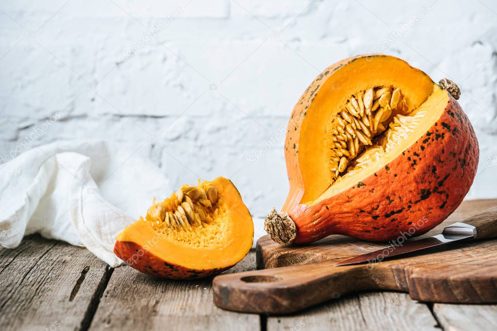 close up view of cut pumpkin on cutting board on wooden surface and white brick wall background