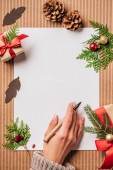 körülvágott kép pen felületen a nő üres papír és díszített karácsonyi ajándék dobozok baubles és örökzöld ágak