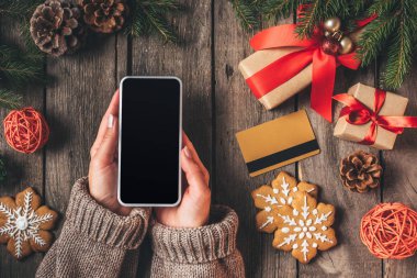 boş ekran ile akıllı telefon ile kredi kartı ve Noel hediyeleri ahşap arka plan üzerinde tutan kadın görünümünü kırpılmış