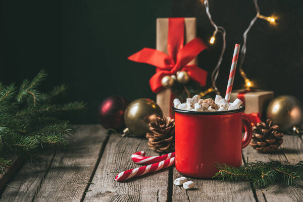cup of hot cocoa with marshmallows on wooden table with christmas fir tree