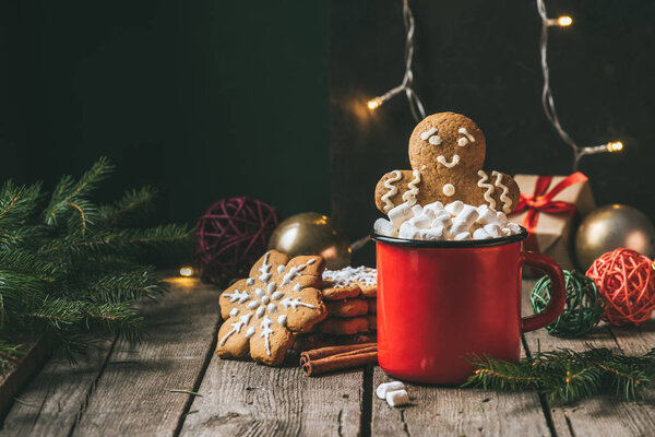 gingerbread man in cup of cocoa with marshmallows on wooden table with christmas light garland