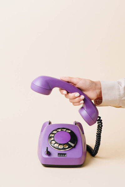обрезанный вид женщины, держащей телефонную трубку фиолетового ротационного телефона на бежевом
