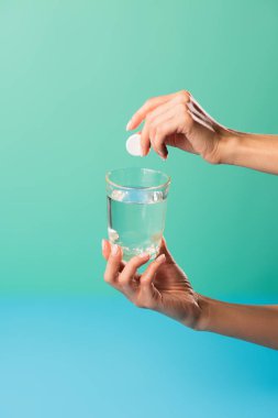 cropped shot of person holding glass of water and pill isolated on green clipart