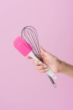 cropped shot of woman holding spatula and whisk isolated on pink clipart