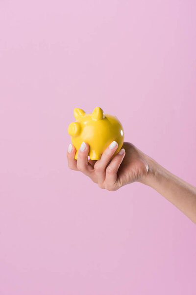 cropped shot of woman holding yellow piggy bank isolated on pink