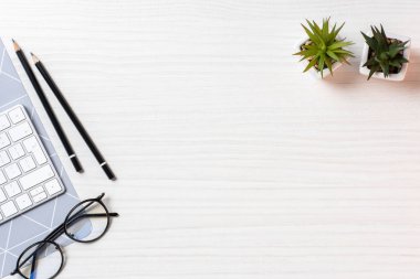 elevated view of workplace with eyeglasses, plants and computer keyboard in office  clipart