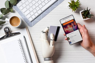 kredi kartı tutan ve Office masada ekranda soundcloud ile smartphone kullanarak protez kol ile işadamı resim kırpılmış 