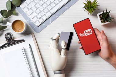 kredi kartı tutan ve ofiste tabloda ekranında YouTube'da ile smartphone kullanarak protez kol ile işadamı resim kırpılmış 