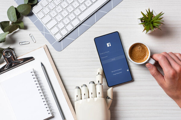 обрезанный образ бизнесмена с протезной рукой с помощью смартфона с YouTube на экране за столом с чашкой кофе в офисе
 