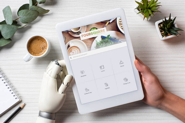 partial view of businessman with prosthesis hand using digital tablet with foursquare on screen at table with coffee cup in office 