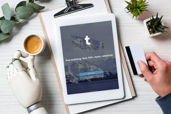 オフィスのコーヒー カップとテーブルで画面に Tumblr とデジタル タブレットを使用し クレジット カードを保持のサイボーグ手で実業家の部分的なビュー — ストック写真