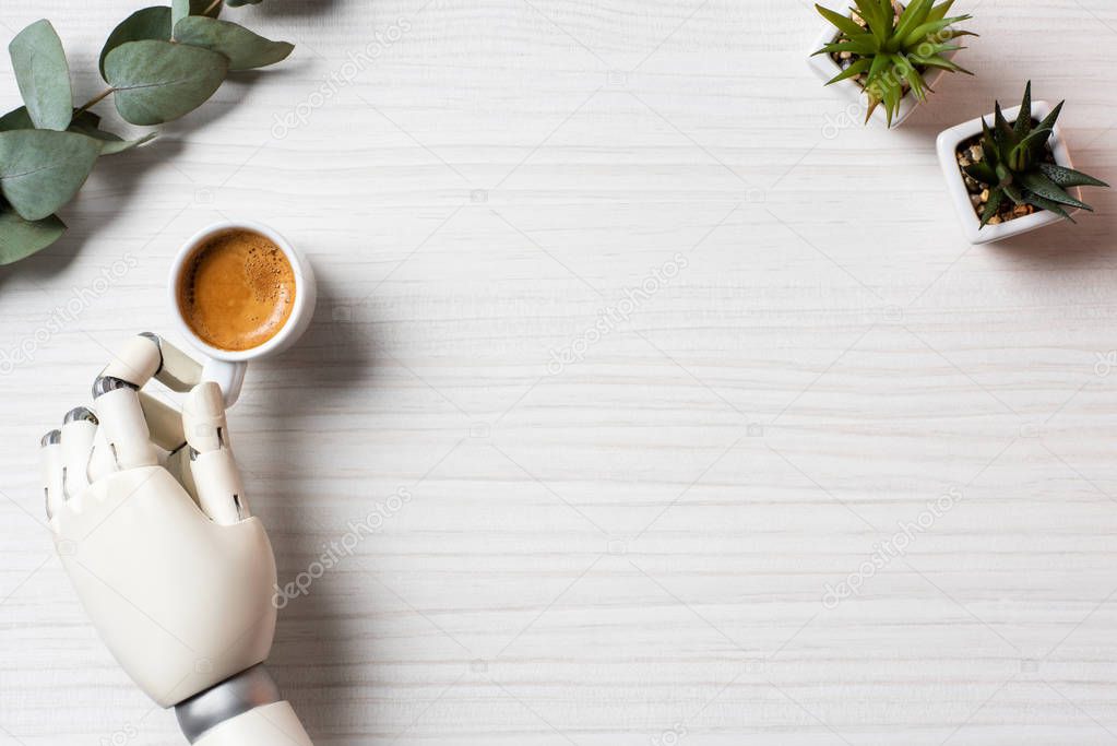 partial view of cyborg hand sitting at table with coffee cup and plants in office 