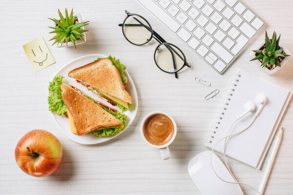 вид на рабочее место с бутербродом, чашкой кофе, яблоком и символом улыбки за столом в офисе
 