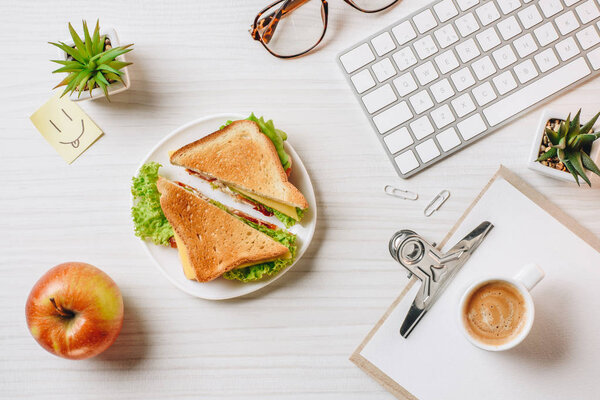 elevated view of workplace with sandwich, coffee cup, apple and symbol of smile at table in office 