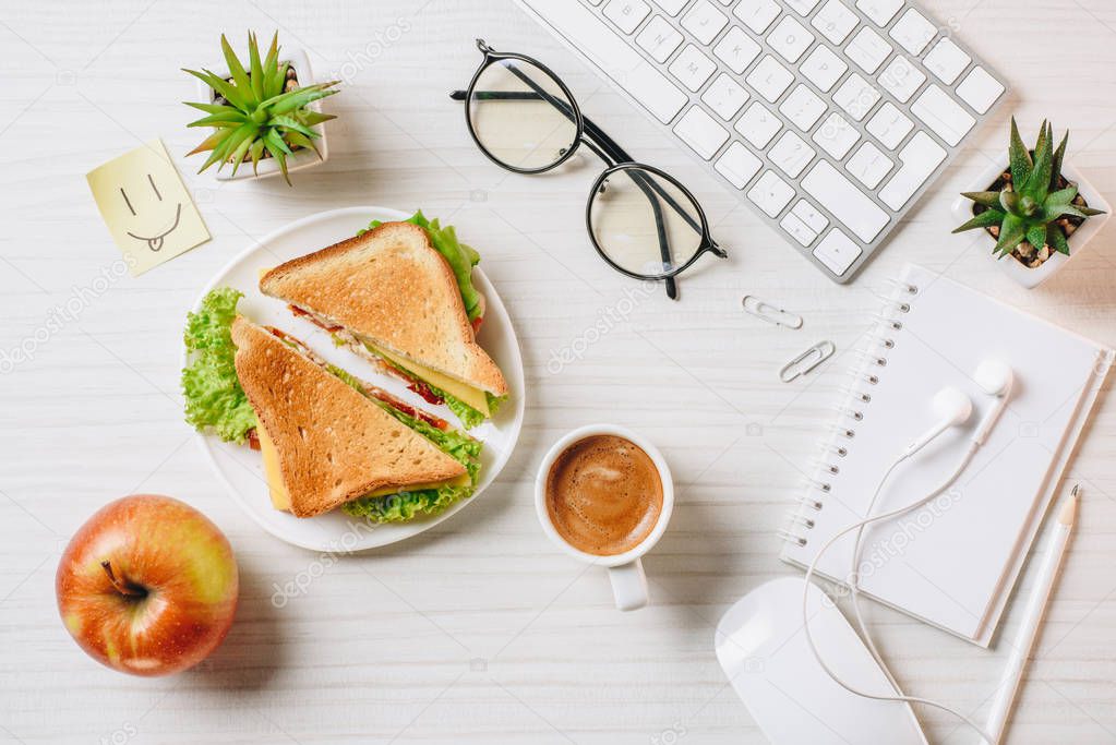 top view of workplace with sandwich, coffee cup, apple and symbol of smile at table in office 